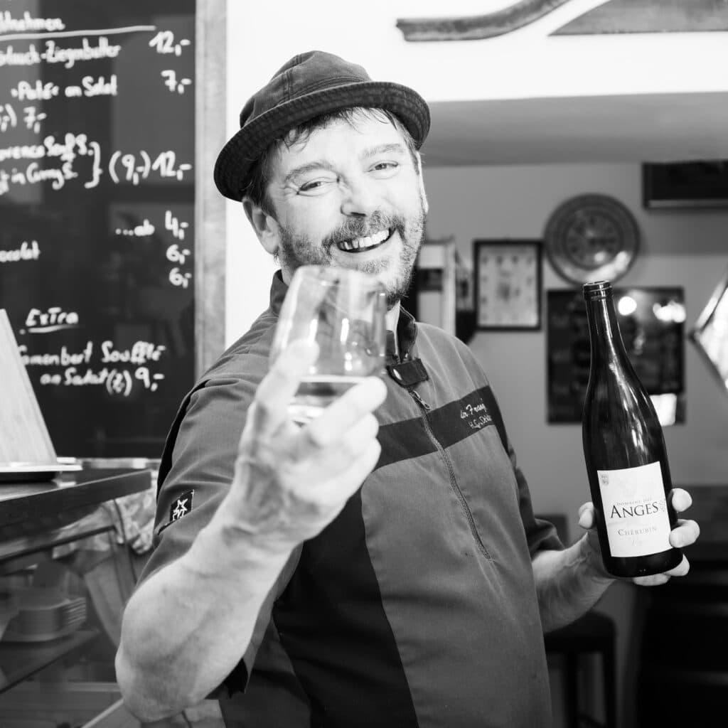 Claude Hervé Leclos, Inhaber von "Der Franzos" in Klagenfurt, hält ein Glas französischen Weißwein in die Kamera