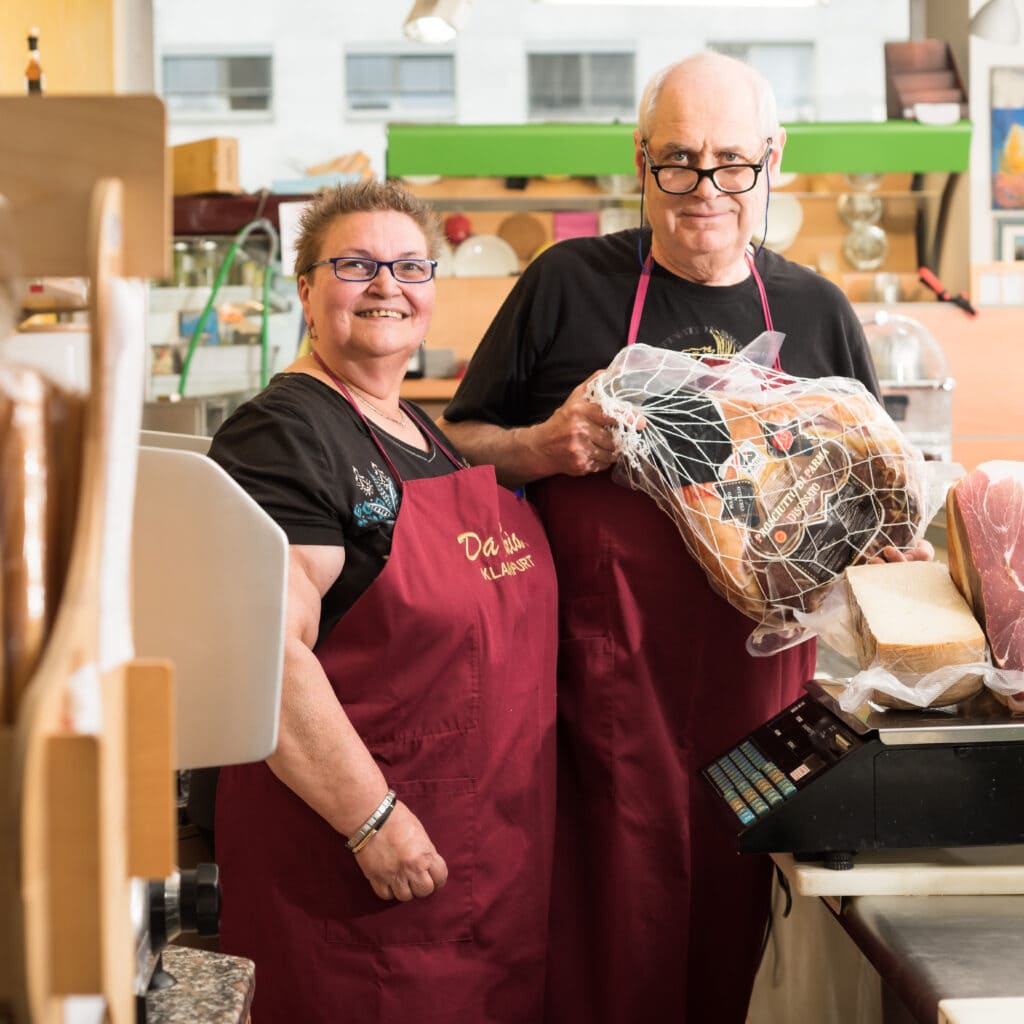 Anna Maria Grotto und ihr Mann mit einem San-Daniele-Schinken und italienischem Käse in ihrem kleinen Lebenmittelgeschäft und Bistro "Da Maria" in Klagenfurt