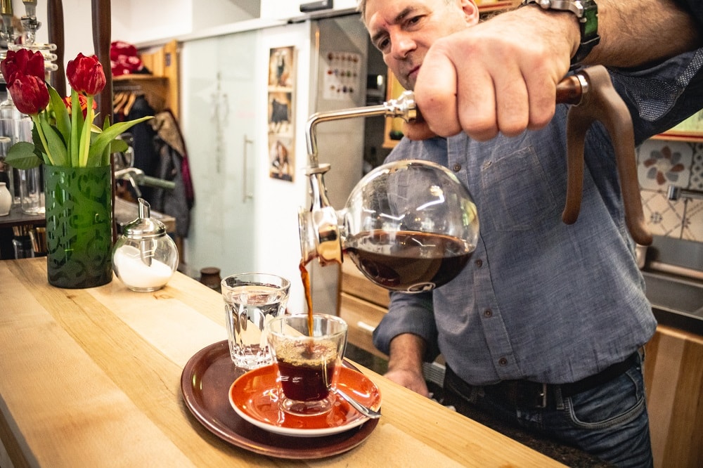 Kellner im Café Lichtspiel in Klagenfurt schenkt Kaffee in eine Glastasse ein
