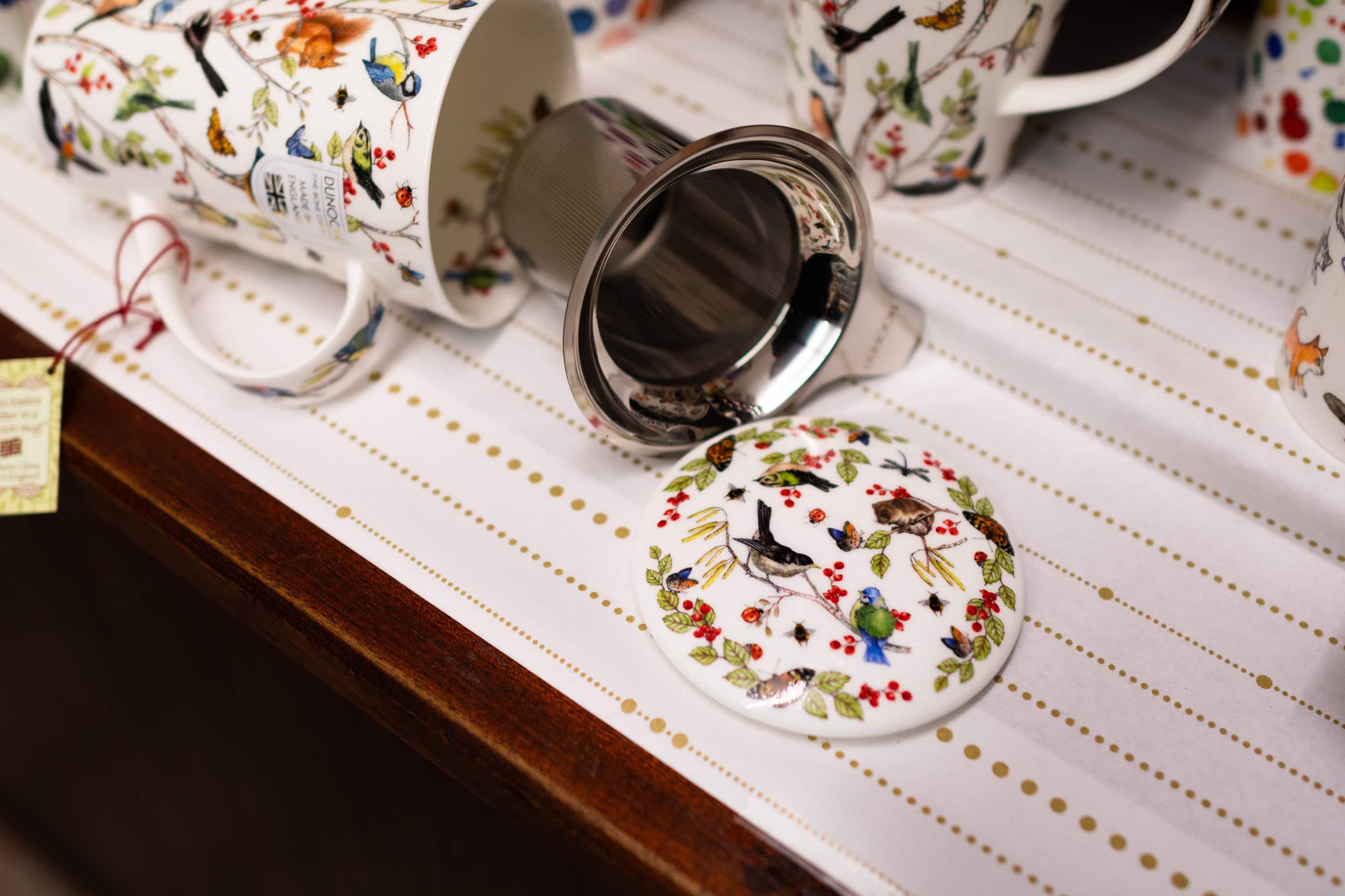 Weiße Teetasse mit bunten Vögeln und Blättern mit Teesudeinsatz bei die Teedose in Klagenfurt