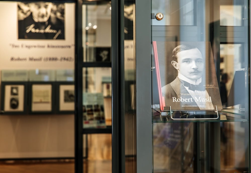 Eingang zum Robert-Musil-Museum in Nahaufnahme. Im Fokus steht ein Buch in der Auslage: "Robert Musil", auch im Hintergrund ist verschwommen ein Portrait von dem Autor an der Wand zu sehen.