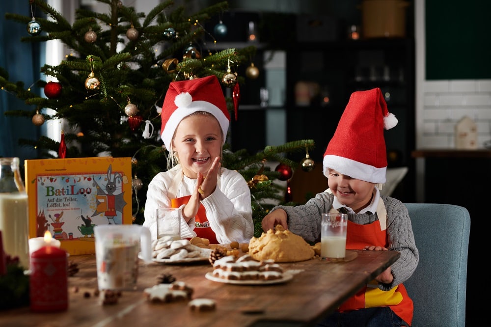 zwei Kinder backen Weihachtskekse und tragen dabei Weihnachtsmützen