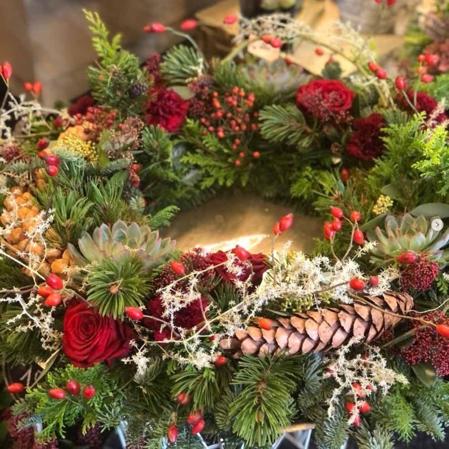 Ein Türkranz aus Naturmaterialien wie Tannenzapfen, Zweige, Hagebutten und roten Rosen von Blumen Margit