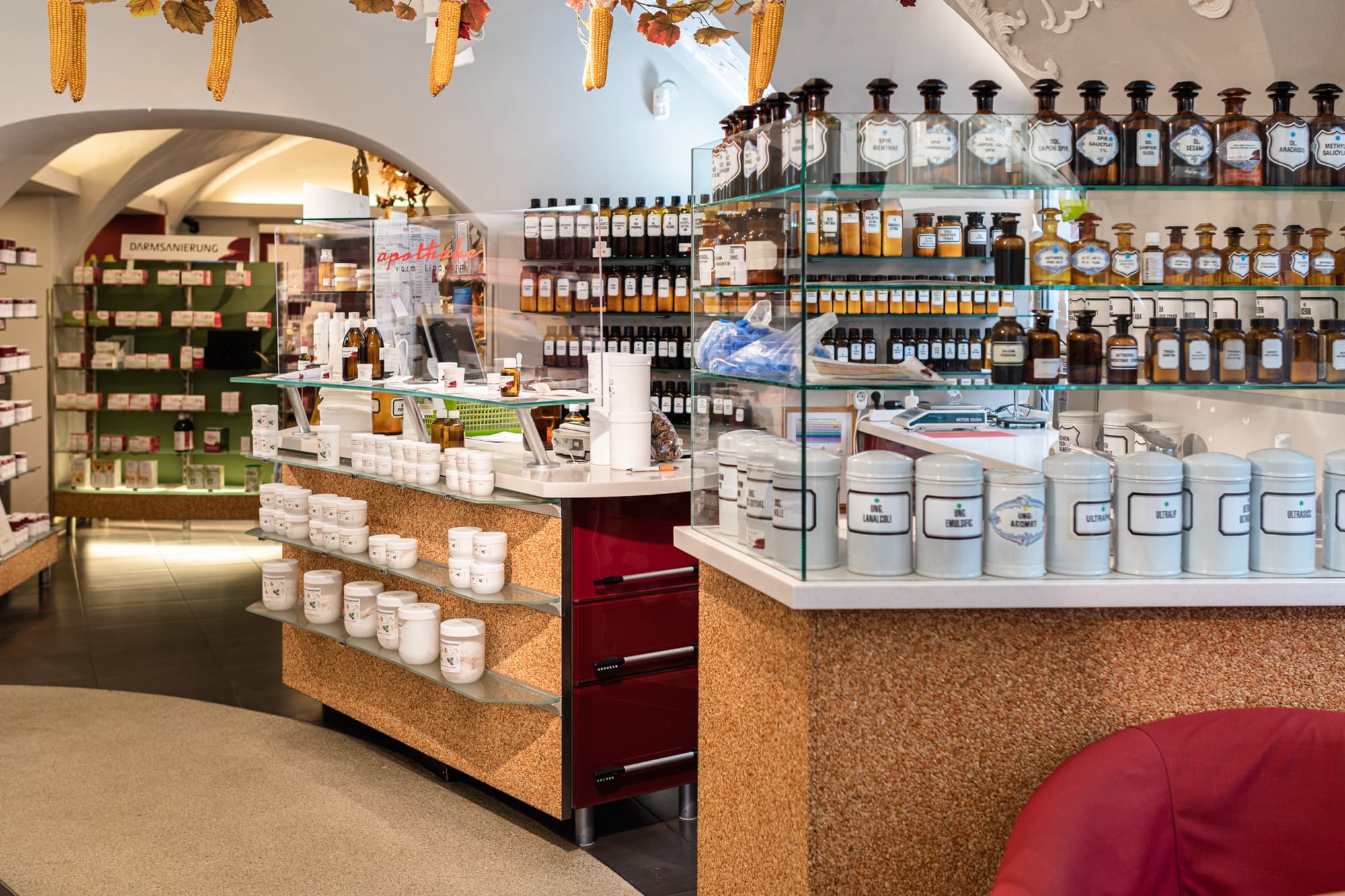 Am Bild ist der Innenraum der Apotheke vorm Lindwurm zu sehen. Hinter einem Tresen sind allerlei Zutaten für die Eigenproduktionen der Apotheke in beschrifteten Flaschen und Behältern zu sehen.
