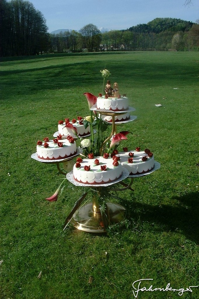 Hochzeitskuchen in weiß mit roten Rosen auf einem goldenen Etagere angerichetet, es steht auf einer grünen Wiese