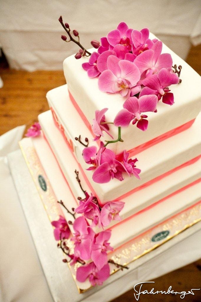eine mehrstöckige Hochzeitstorte, wie eine Treppe modelliert mit weißem Fondantüberzug und pinken Orichideen geschmückt