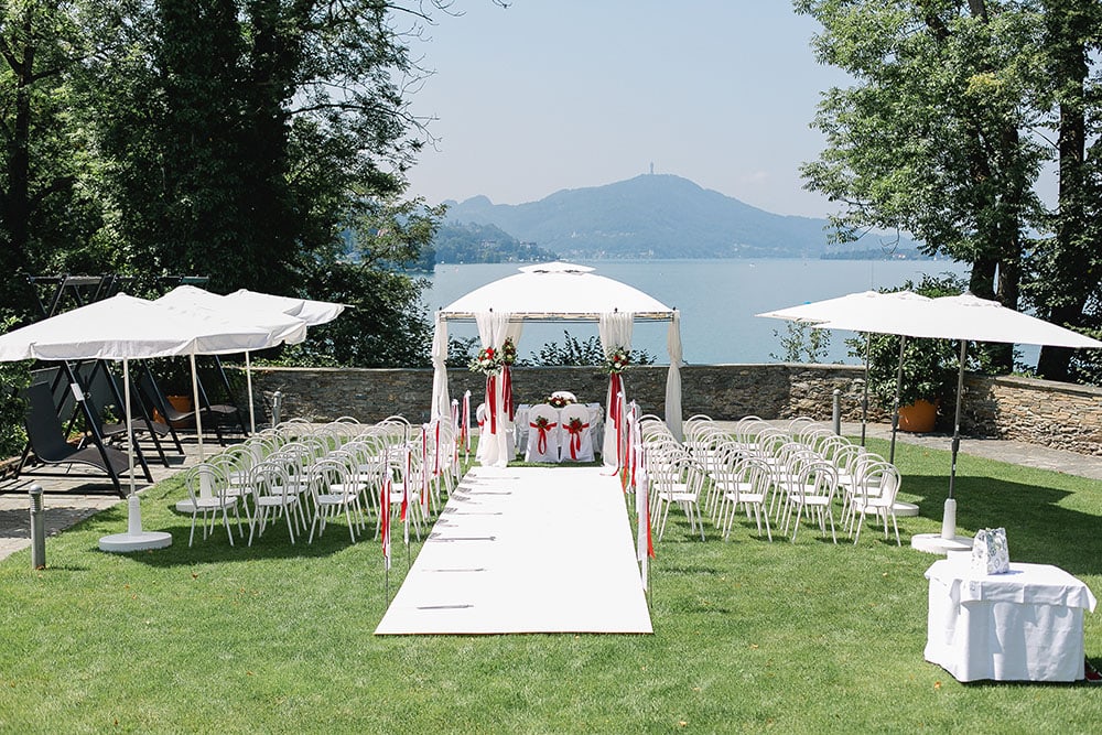 die open air hochzeitslocation direkt am Wörthersee, das Schloss Maria Loretto, auf der Schlosswiese ist ein weißer Steg für das Brautpaar mit Pavillon und die Bestuhlung für die ganze Hochzeitsgesellschaft hergerichetet, im Hintergrund ist der Wörthersee zu sehen