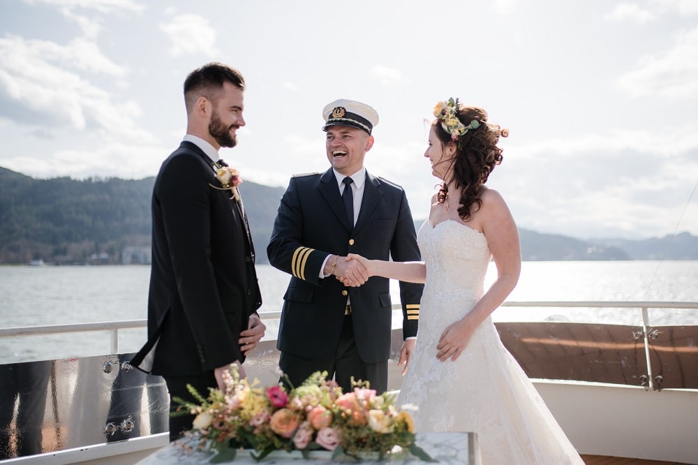 ein Brautpaar wird auf einem Schiff der Wörtherseeschifffahrt getraut, der Kapitän gratuliert der strahlenden Braut mit Handschlag