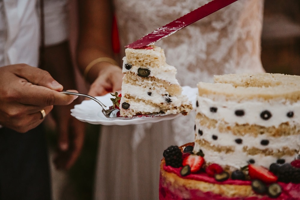 ein Brautpaar hat die Hochzeitstorte angeschnitten und sie verteilen das erste Stück der mehrschichtigen Cremetorte