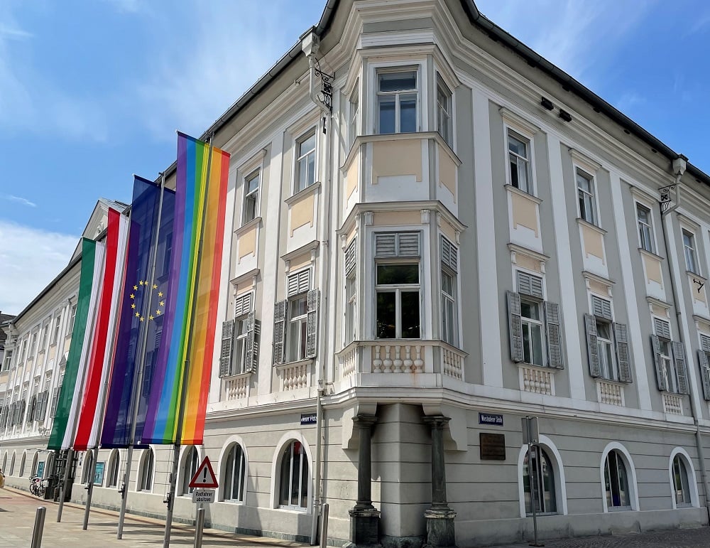 Fasade des Rathauses in Klagenfurt mit gehissten Flaggen von Italien, Österreich, Europa und der Regenbogenflagge