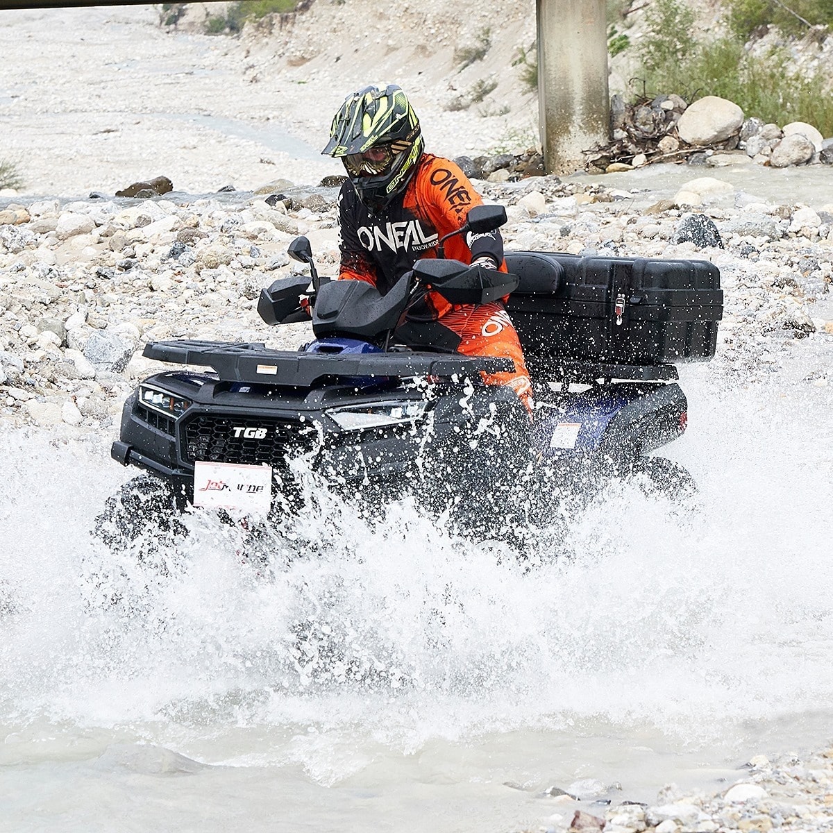 ein Mann fährt mit einem Quad und Schutzkleidung durch einen Bach