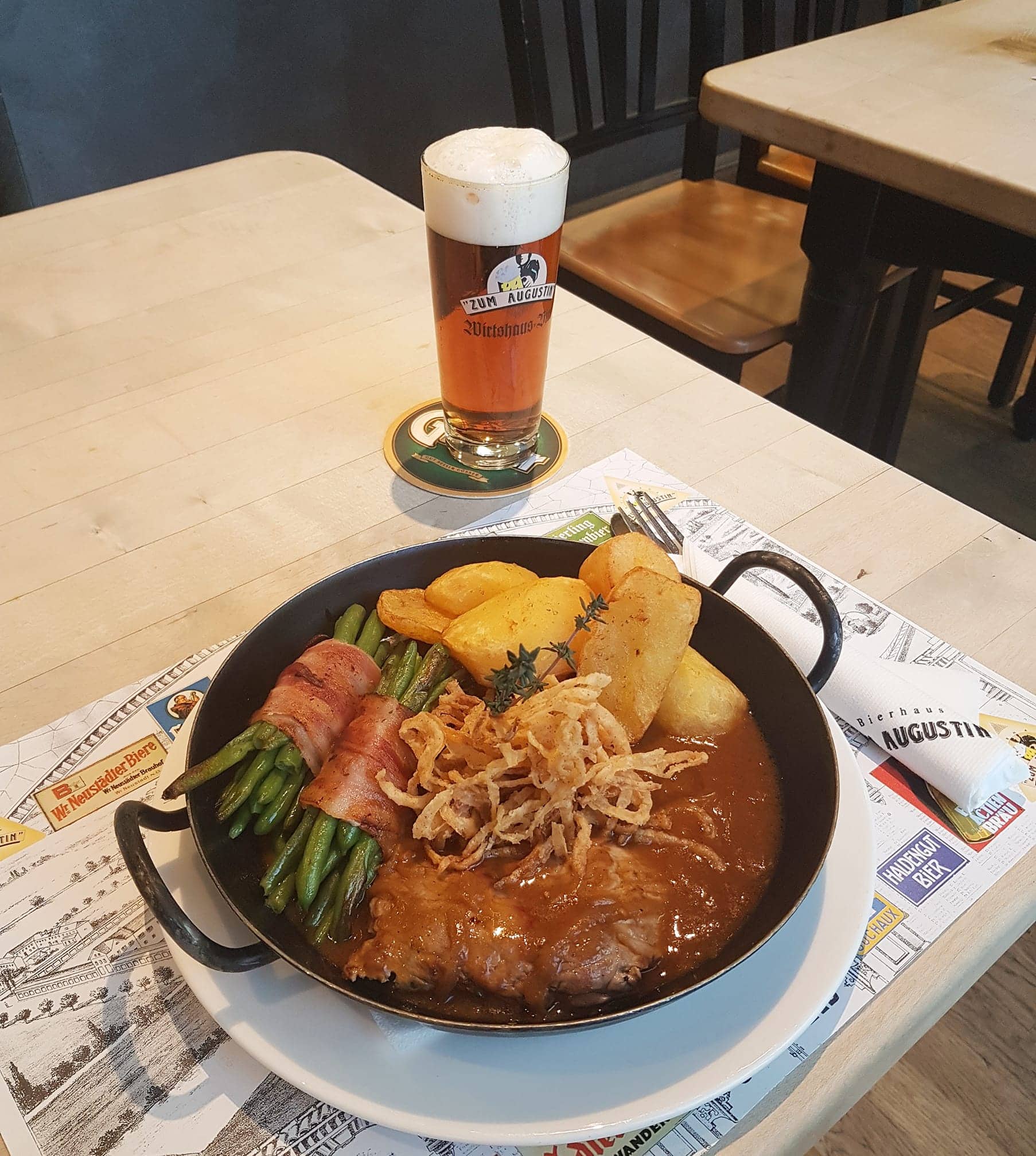 Zwiebelrostbraten in einer gusseisernen Pfanne serviert, dazu gibts Bohnen im Speckmantel und Kartoffelspalten, im Bierhaus zum Augustin