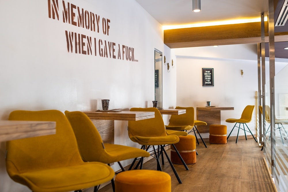 Blick in das Café Karl mit braunen Bistrotischen und senfgelben Stühlen, sowie Hockern, an der Wand ein Spruch: in memory of when I gave a fuck