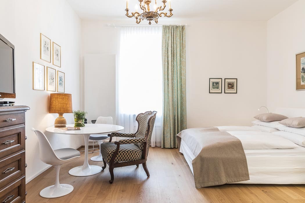 elegantes Zimmer mit großem Doppelbett und weißem runden Tisch im Palais Musil in Klagenfurt
