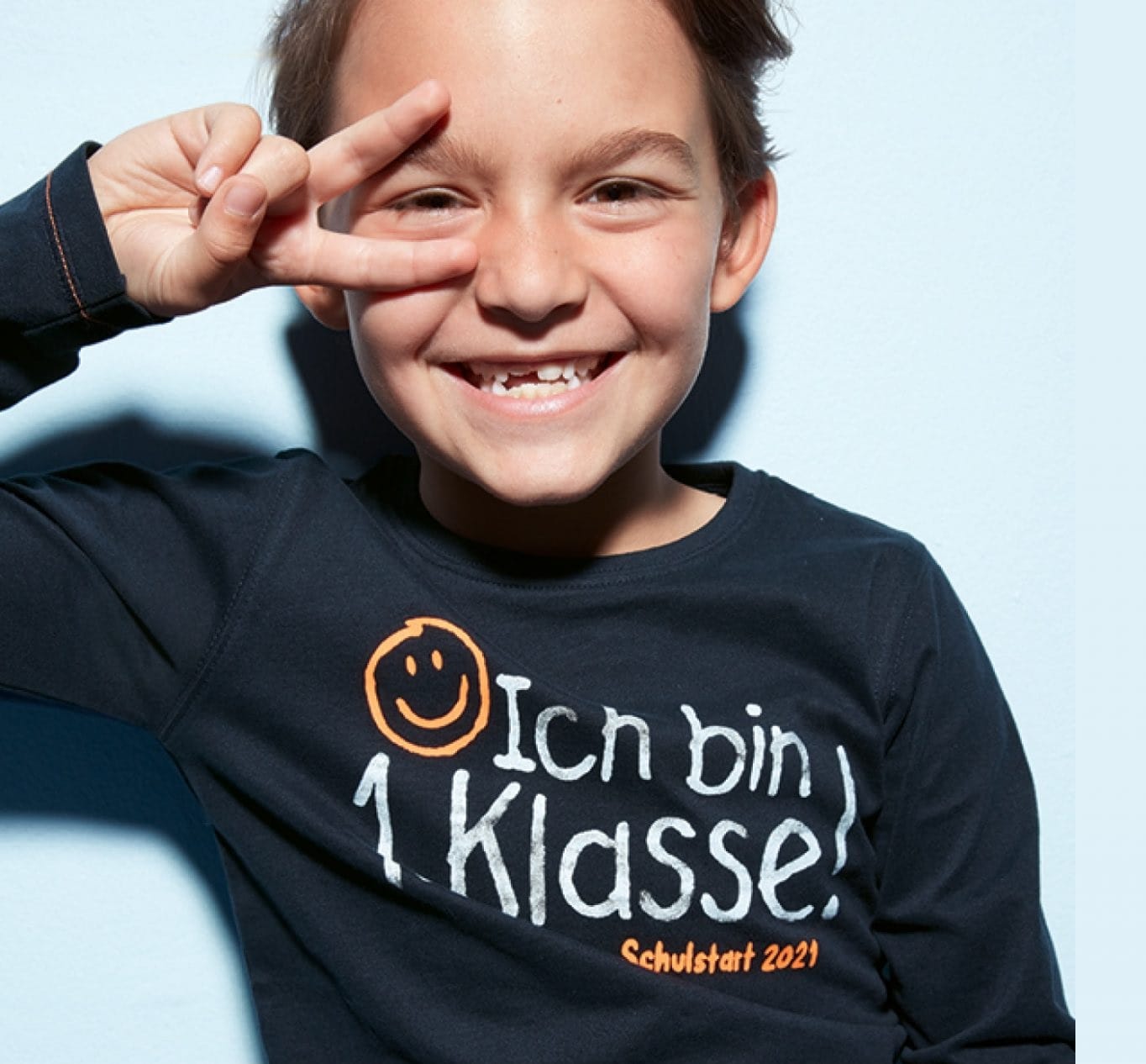 ein Bub trägt ein schwarzes Shirt mit der Aufschrift "ich bin 1. Klasse" zum Schulbeginn