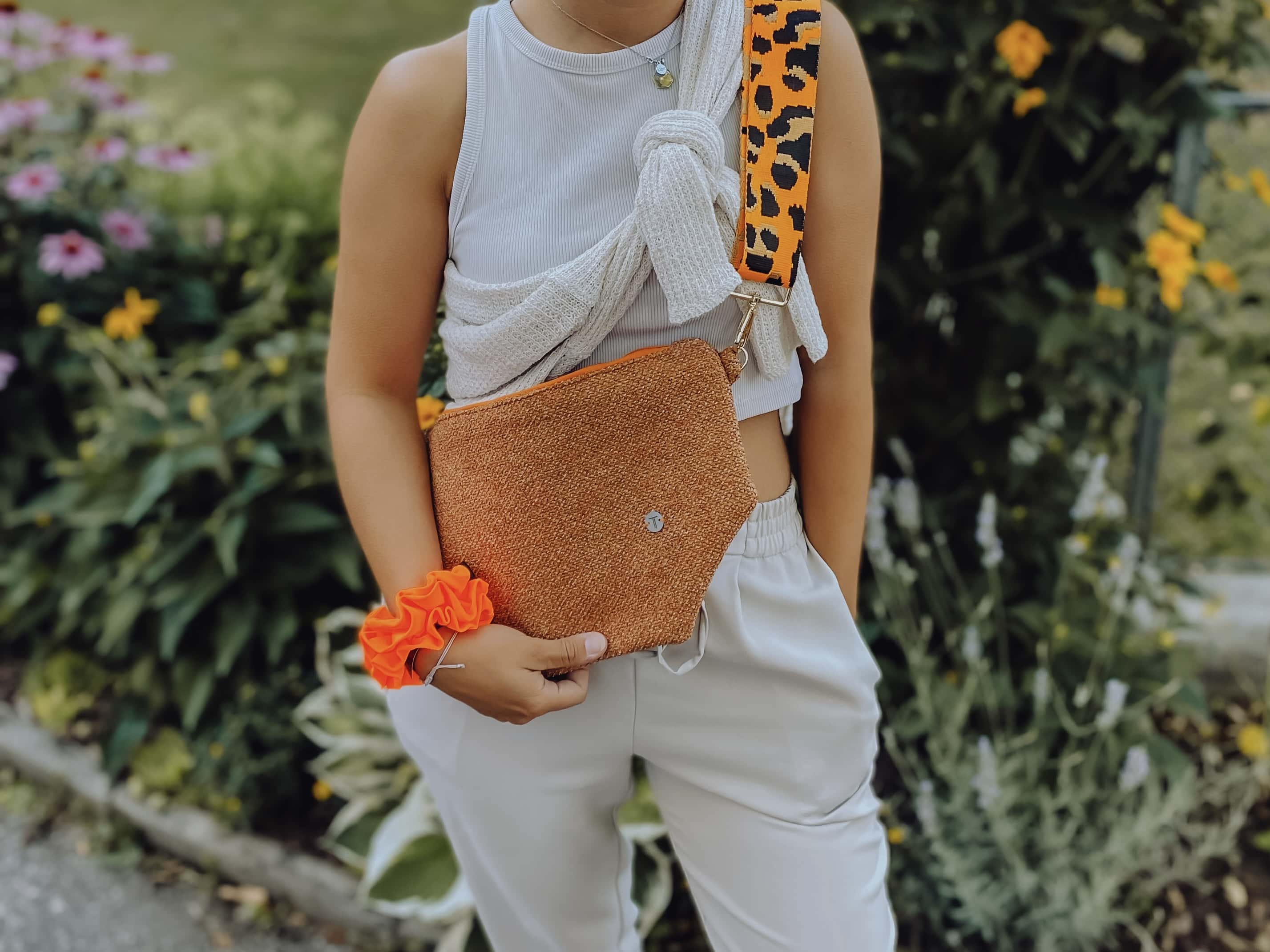 Eine Frau präsentiert eine orange Tasche und ein oranges Haarband am Hansgelenk von TINKA