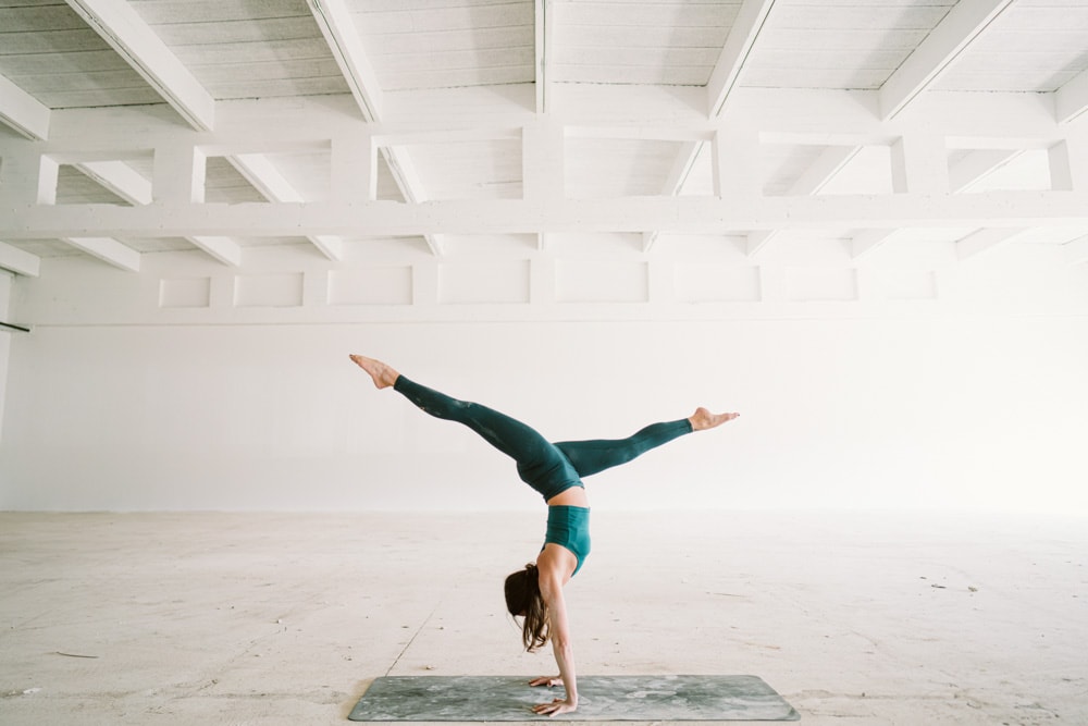 Nicoya Yoga - Yogi in dunkelgrünem Yoga Set macht Handstand