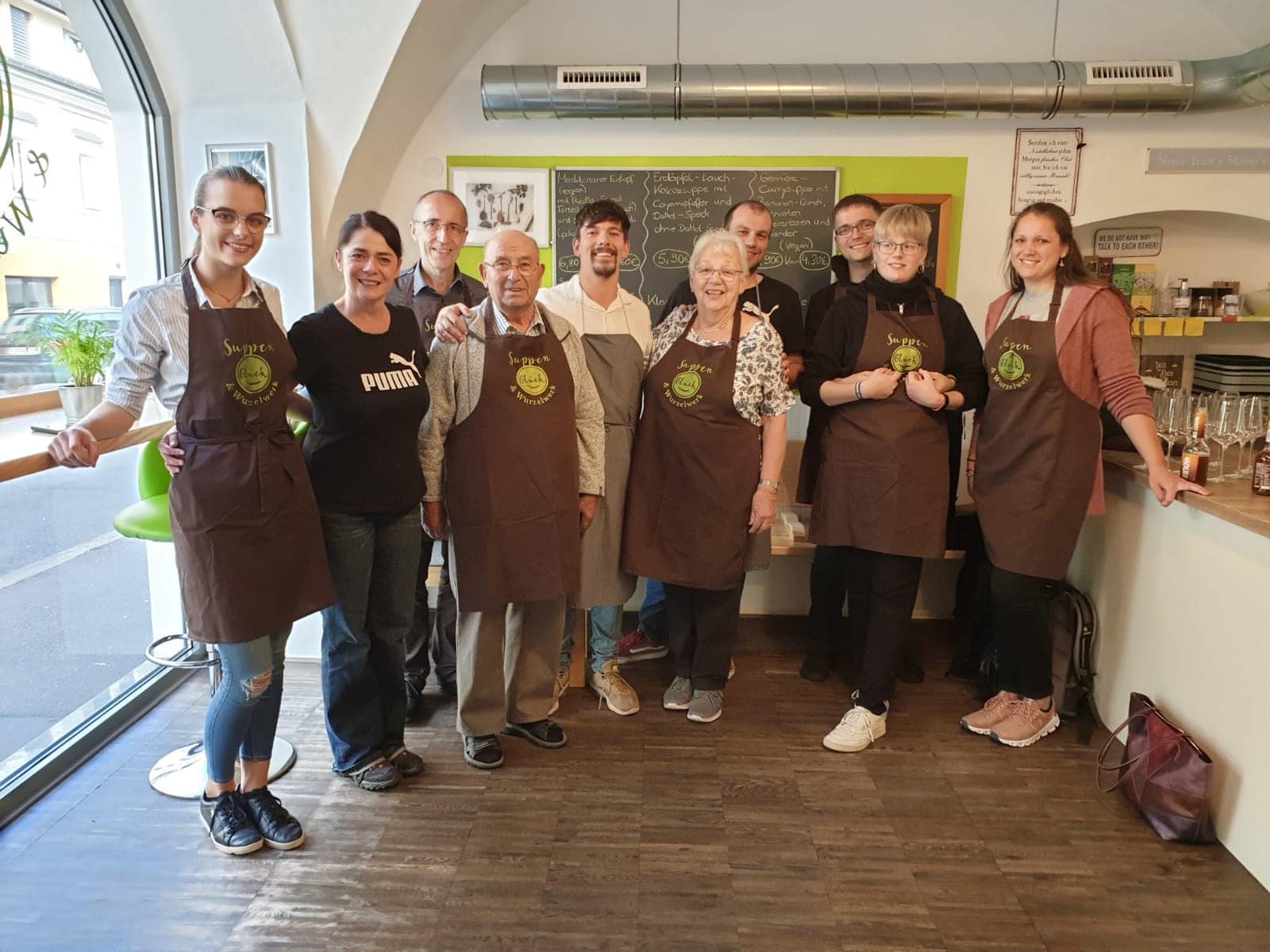 ein erfolgreicher Kochkurs bei Suppenglück in Klagenfurt, alle Teilnehmer strahlen in die Kamera und tragen Suppenglück-Kochschürzen