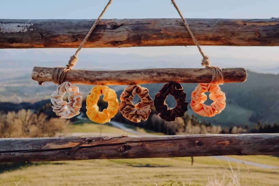 Haarbänder, Scrunchies der Firma Tinka aus Klagenfurt, handgemacht in verschiedenen Farben beige, gelb, braun, orange, caramel hängen auf einem Ast aufgewickelt, im Hintergrund eine Berglandschaft