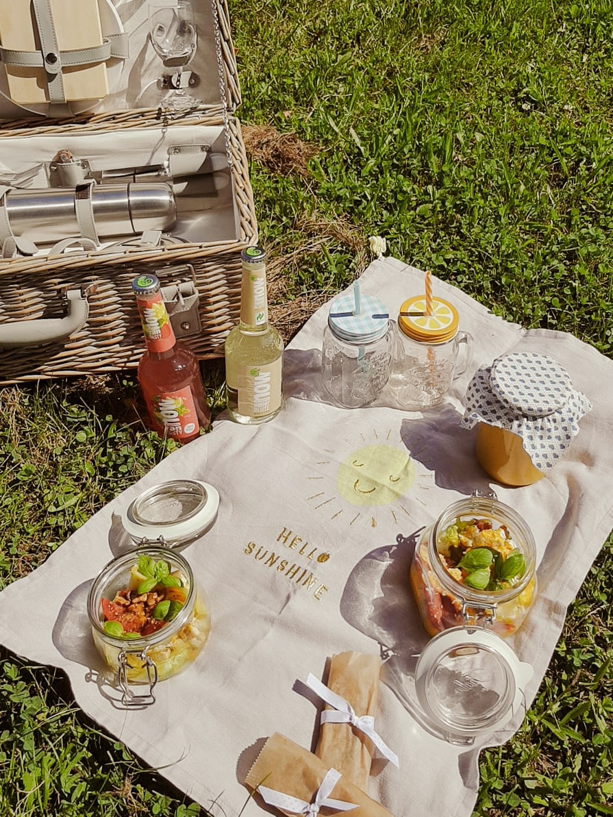 Picknickdecke mit Regläsern gefüllt mit jungem Marktsalat, Mango und gebratenem Tofu