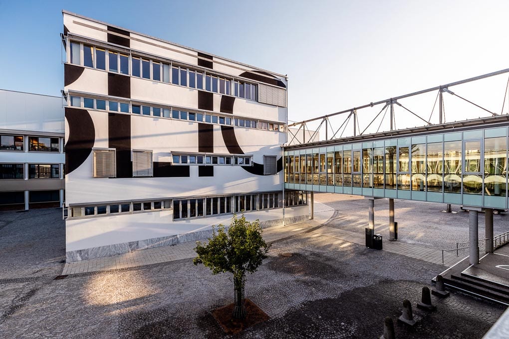 Die Bibliothek der Alpen Adria Universität Klagenfurt von außen. Auf dem weißen "Kubus" steht in großen schwarzen Buchstaben um die Ecken "Bibliothek" 