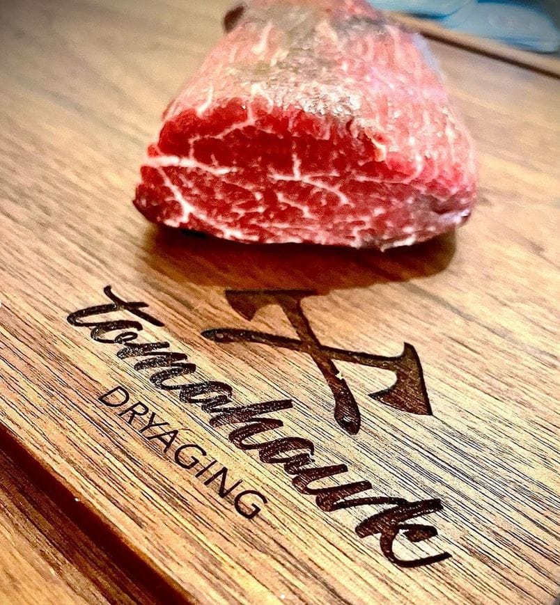 ein rohes Steak auf einem Holzbrett mit der Aufschrift tomahawk dryaging vom Lokal Wohnzimmer bzw. Freiraum in Klagenfurt