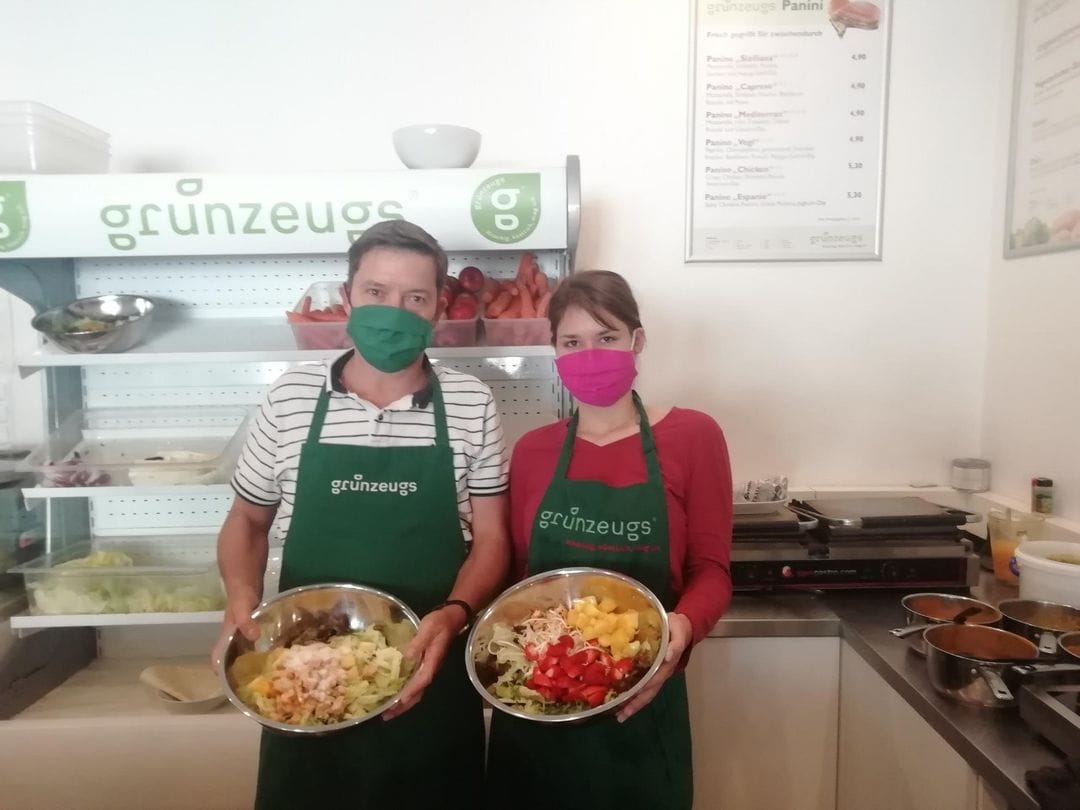Salate und Suppen beim Grünzeugs Klagenfurt auch to-go, am Foto sind zwei Mitarbeiter des Lokals, ein Mann und eine Frau mit Maske und jeweils einer Schüssel mit Zutaten für die Gerichte