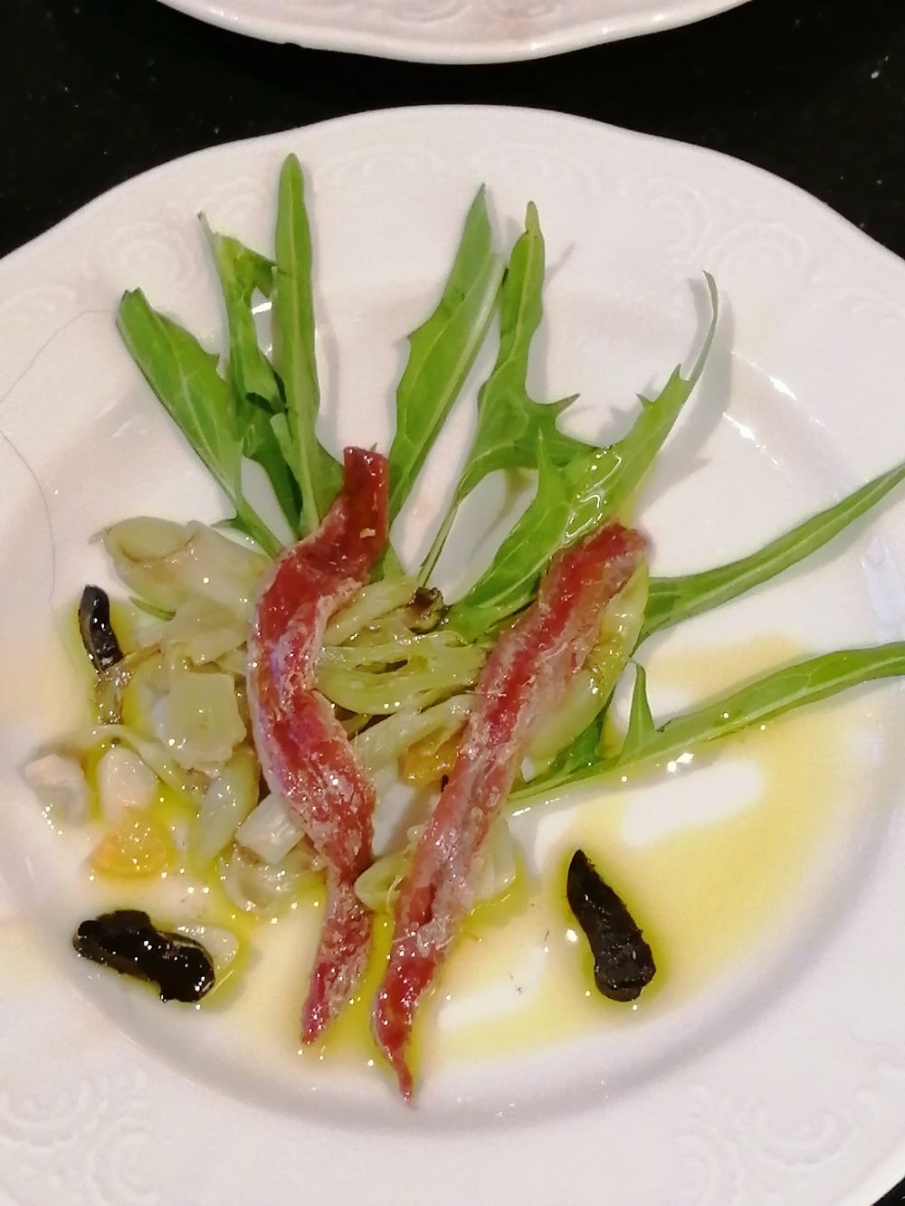 punterelle Sardellen, schwarzer Knoblauch und Rucola mit Olivenöl auf einem weißen Teller angerichtet
