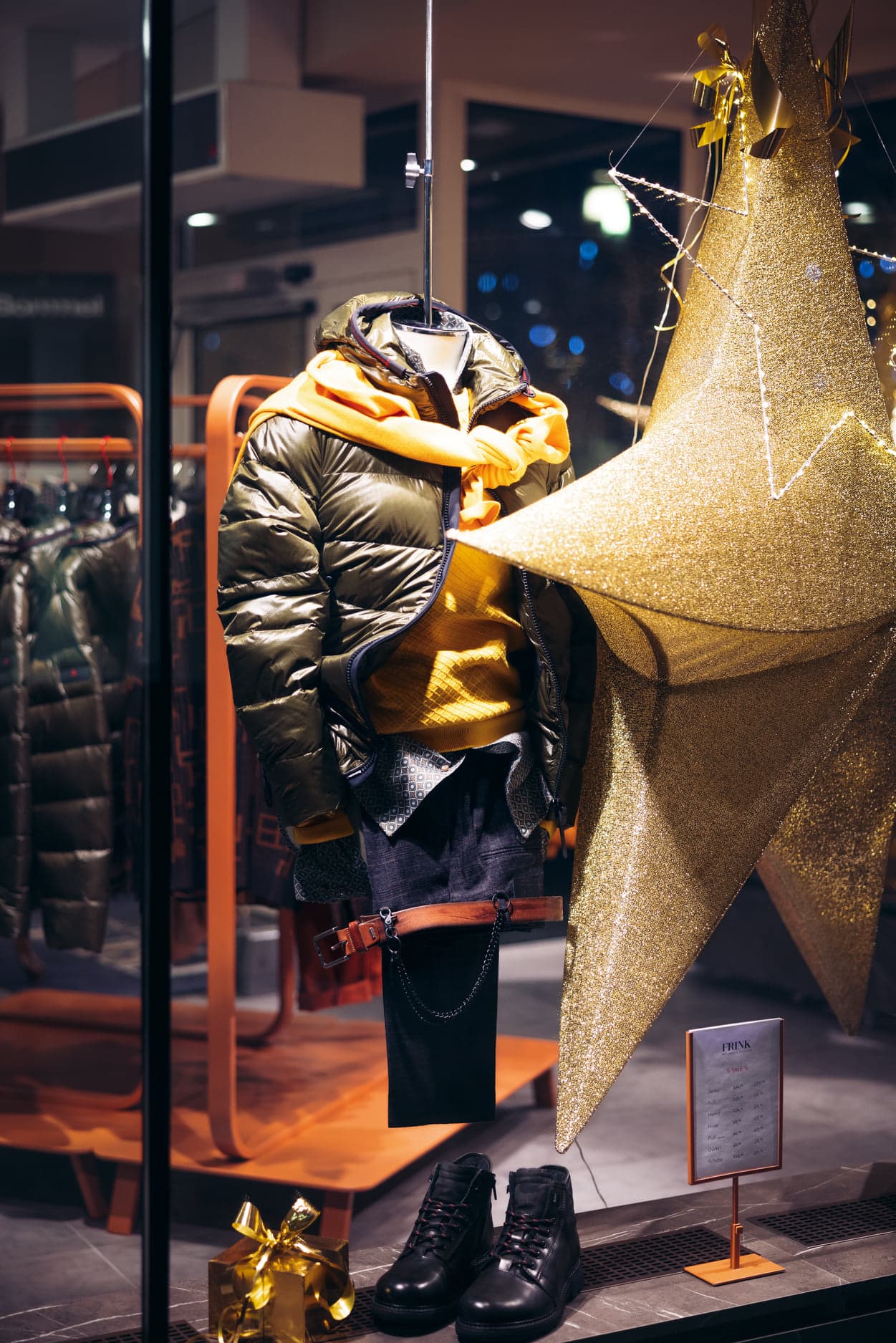 Herren Winteroutfit mit Daunenjacke, senffarbenem Pullover und Schal, Jeans mit einem brauen Gürtel von Frink Mode in Klagenfurt, Pernhartgasse