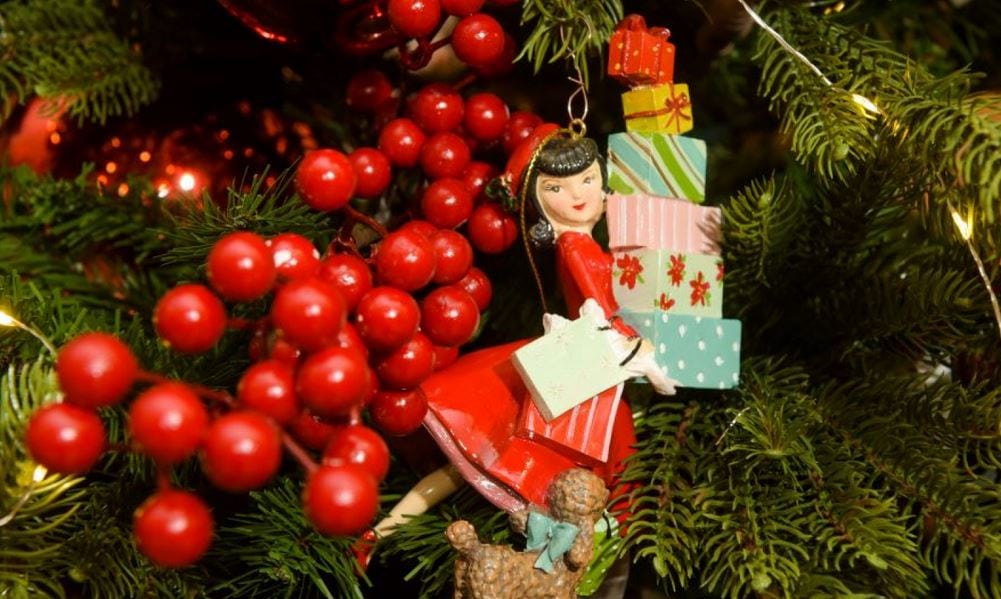 Ein Christbaumanhänger in Form eines Mädchens, das einen Stapel mit Geschenken trägt von Casa Viva in Klagenfurt
