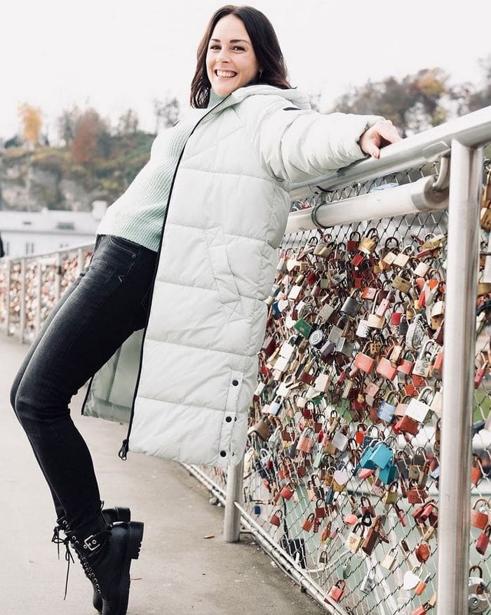 weißer Daunenmantel von Kleiderbauer, er wird auf einer Brücke mit Schlössern präsentiert