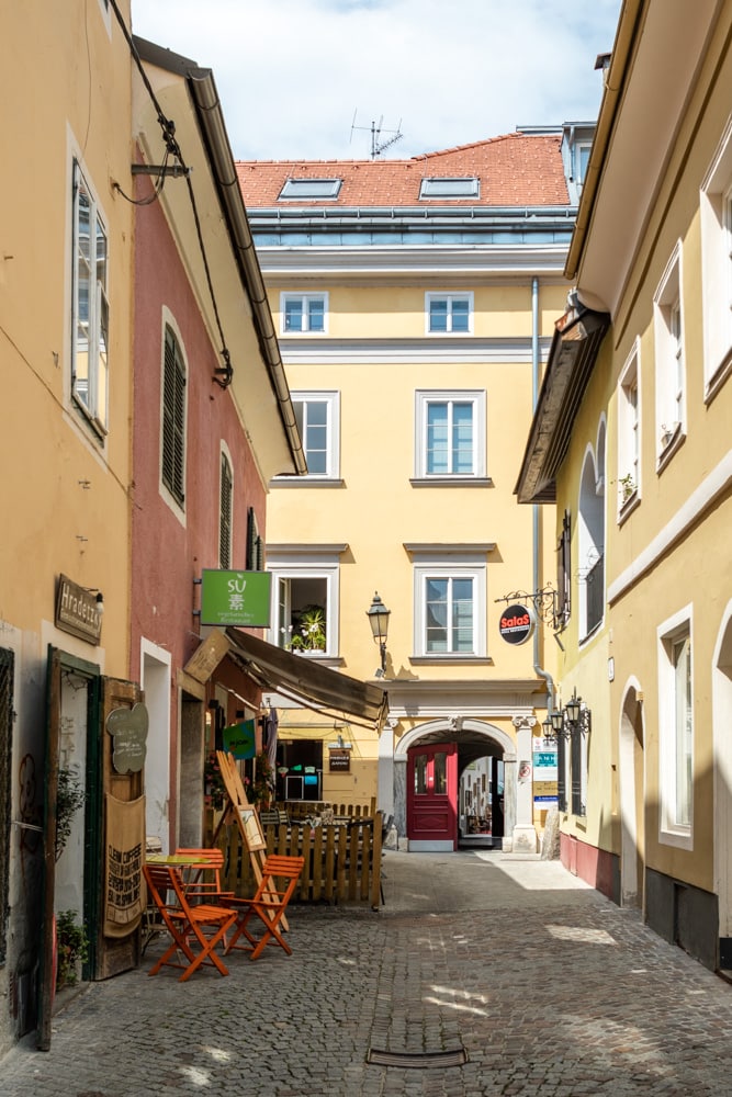 Die Badgasse nach Norden hin fotografiert, die Sonne scheint auf die Fassade der Häuserreihe rechts, die linke ist im schatten, man erkennt Schilder von Hradetzky und dem Restaurant SU, beim Haus am Ende der Gasse ist ein Borgentor