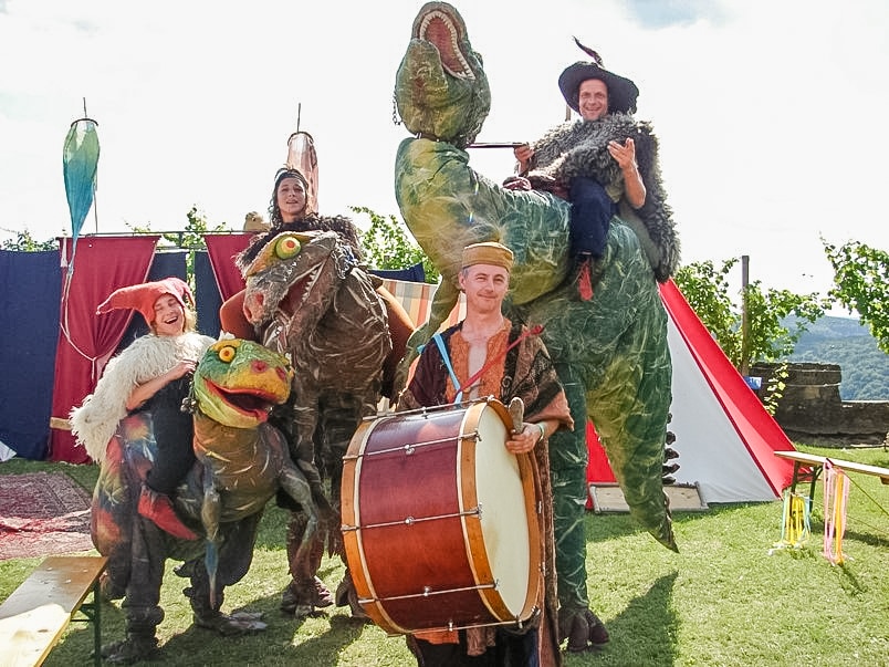 Vier Personen in Verkleidung - drei als Dino oder Drachen einer mit Kappe und großer Bauchtrommel. Ein 