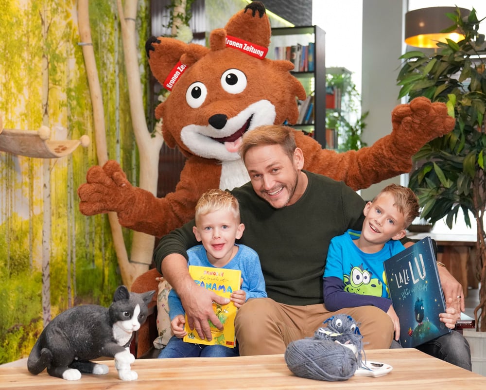 Leseonkel Christian Krall liest im Katzencafé, bei ihm sitzen zwei begeisterte Kinder und hinter ihnen steht der Lesefuchs Theo
