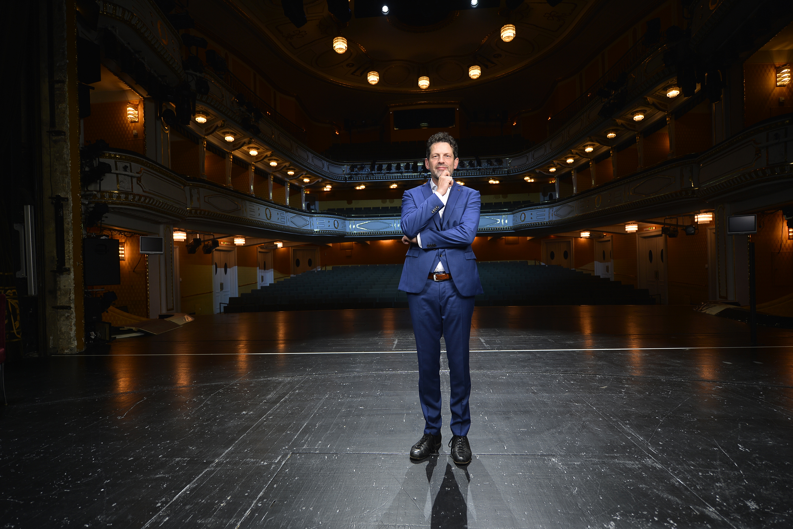 Stadttheater von innnen. Sitzplätze, Bühne. Mann im blauen Anzug im Vordergrund