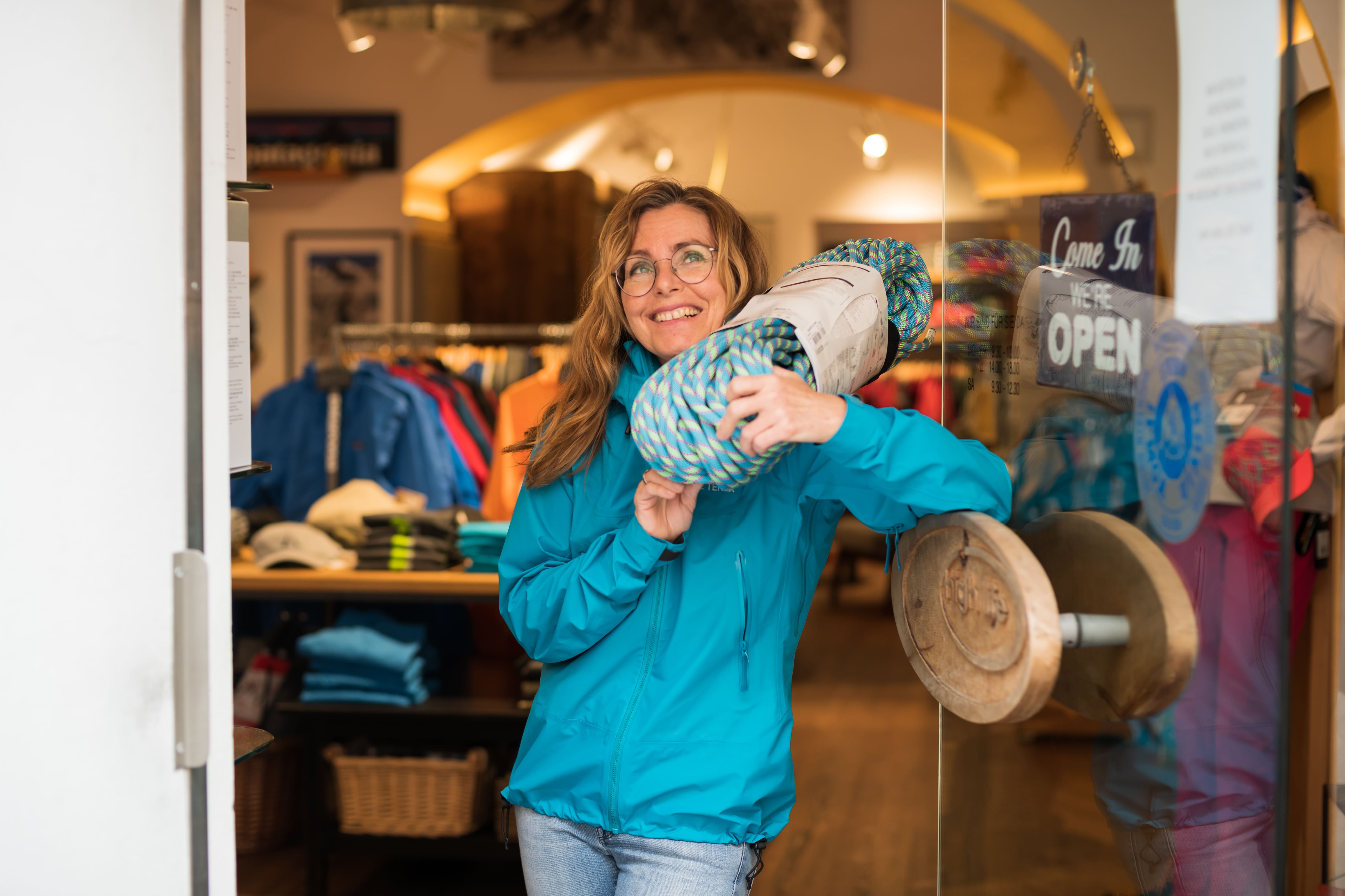 Brigitte Obiltschnig, GF von High Life in Klagenfurt, steht am Geschäftseingang, schultert ein Kletterseil und lächelt freundlich