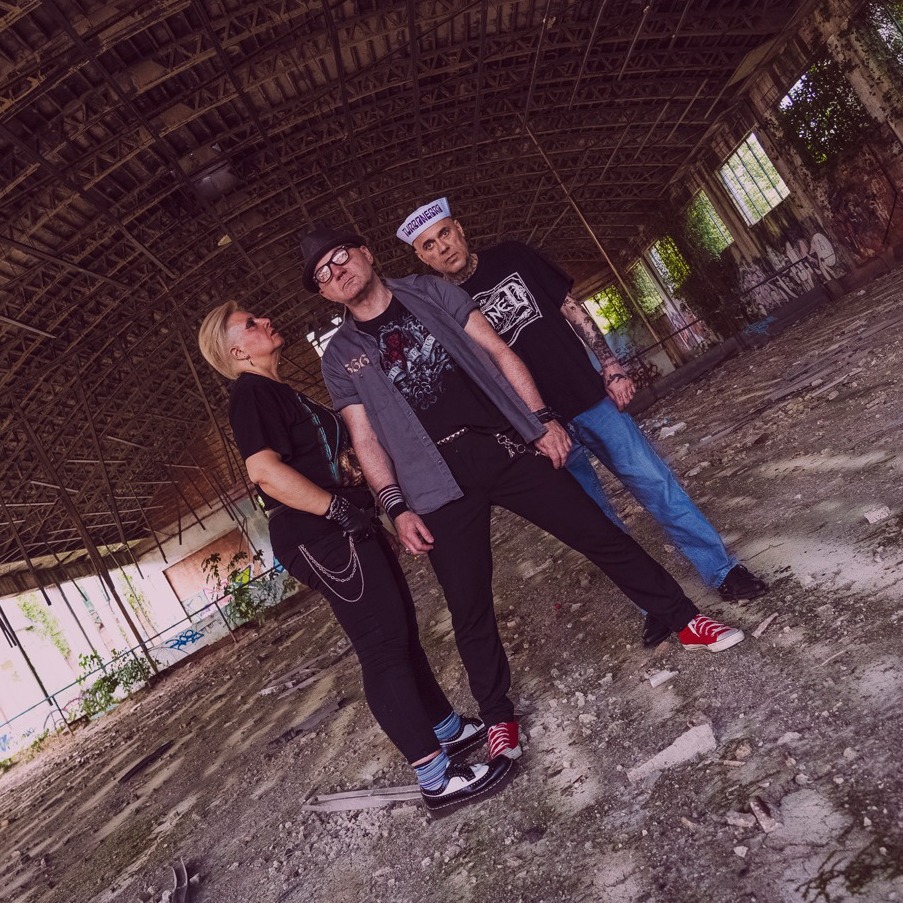 Die Mitglieder der italienischen Punkband "Magic Jukebox" - zwei männliche und eine weibliche Musikerin - stehen dicht aneinander in einer alten, halb verfallenen Halle