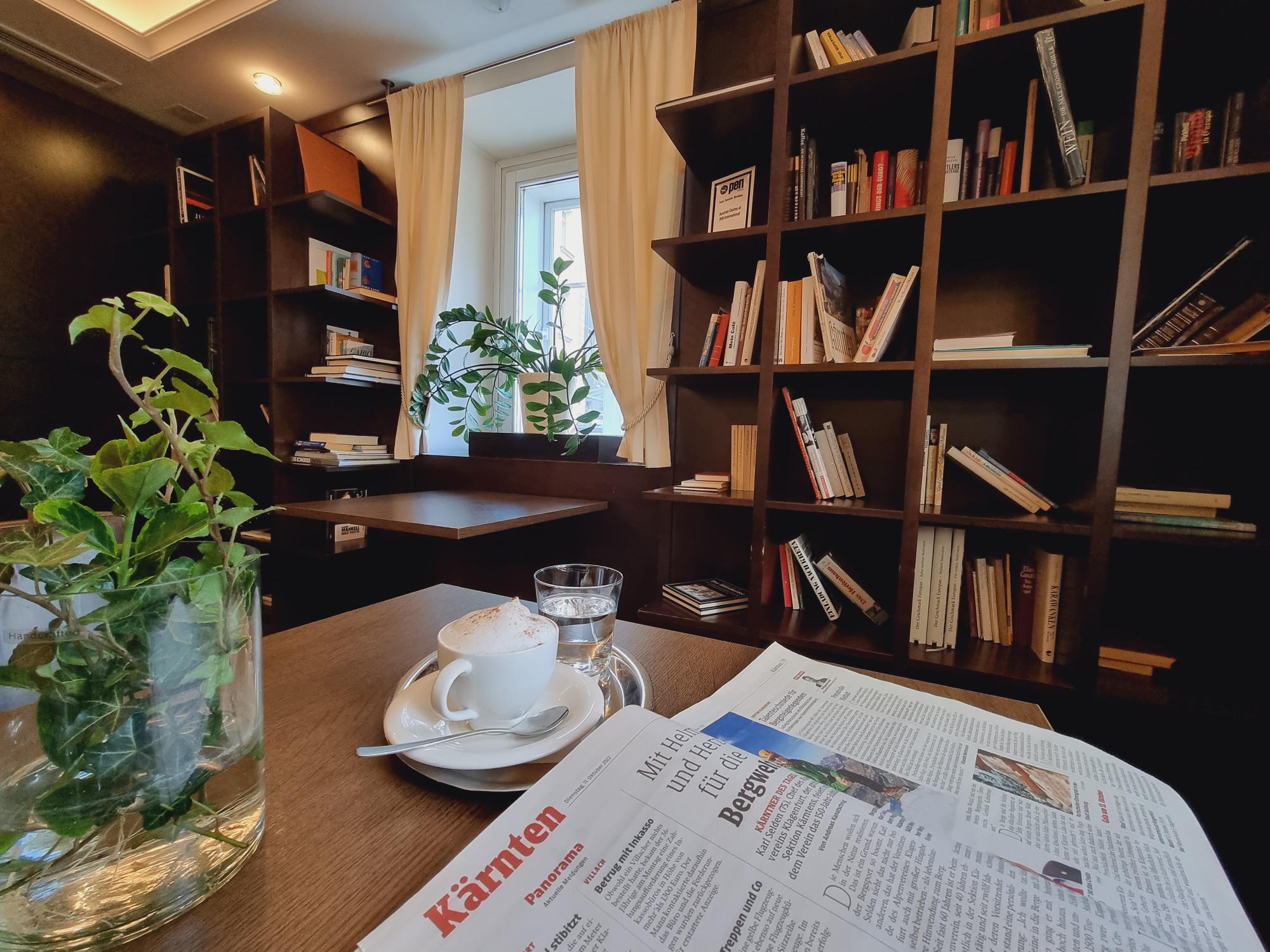 Die Bücherlounge im Cafe Sandwirth mit aufgeschlagener Zeitung, Kaffee und dem Bücherregal im Hintergrund