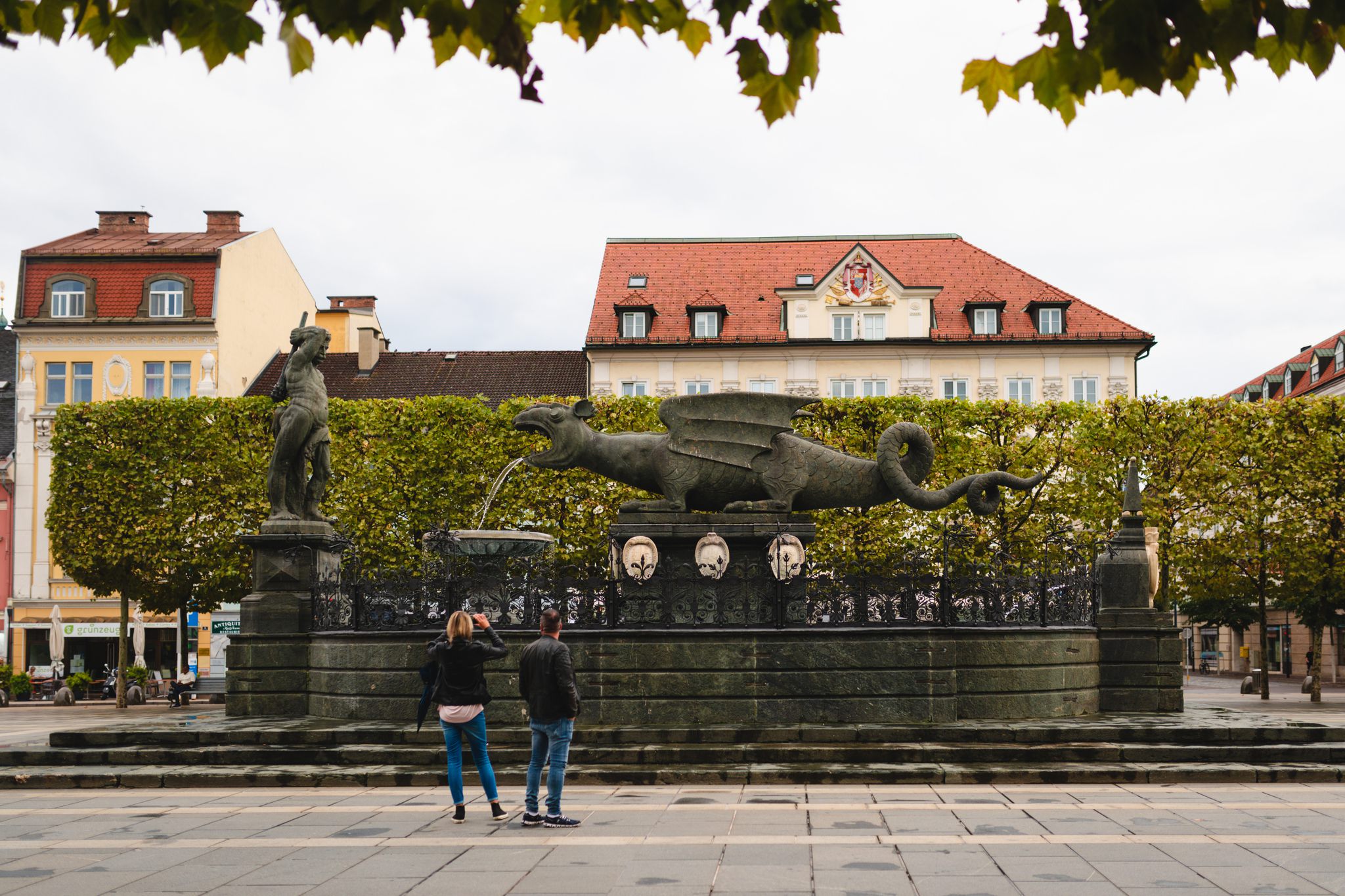 Lindwurm am Neuen Platz in Klagenfurt am Wörthersee mit zwei Touristen, die davon ein Foto machen 