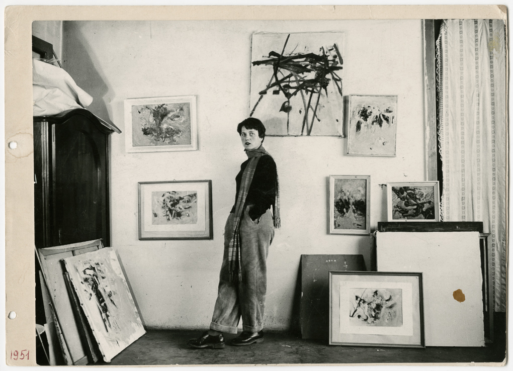 Maria Lassnig stehend vor ihren Werken im Atelier 