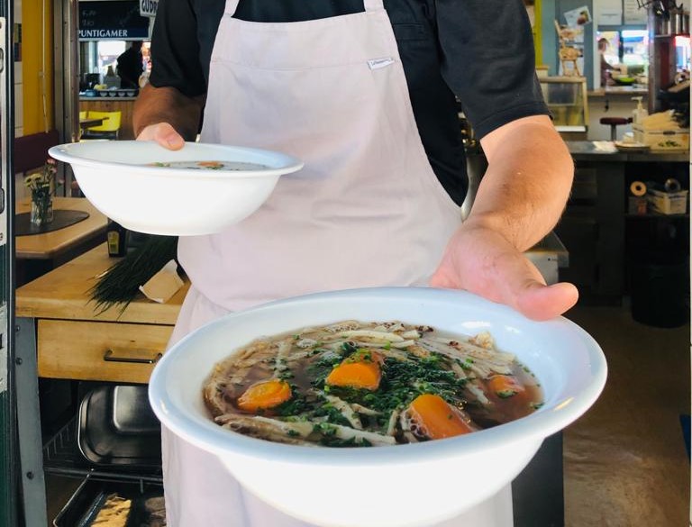 Ausschnitt eines Kochs mit Kochschürze, der einen Teller Fritattensuppe in Klagenfurt in die Kamera hält