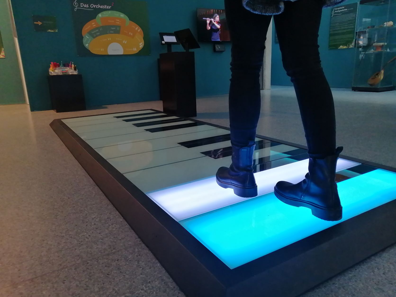 Junges Mädchen steht auf dem Bodenklavier der Ausstellung MusiKUSS im Mitmach-Museum Wissenswertwelt, zwei Tasten leuchten