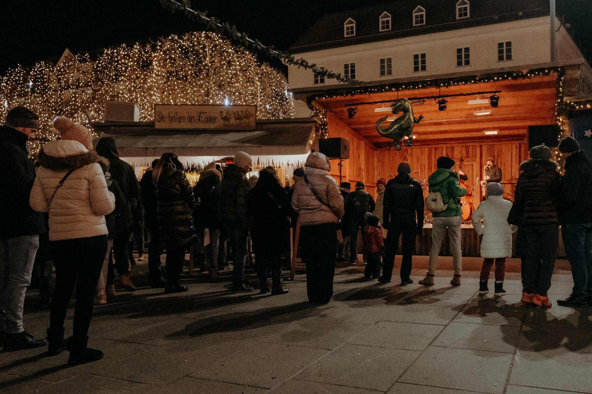 Menschen von hinten vor der bespielten Bühne am Christkindlmarkt Klagenfurt