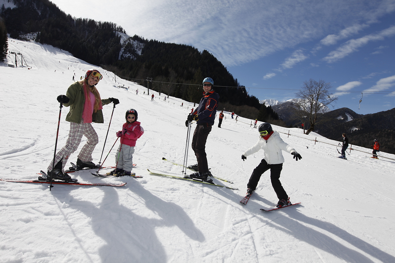 Eine Familie - Elter mit zwei Kindern - stehen in Skiern auf der Piste im Bodental und lächeln in die Kamera