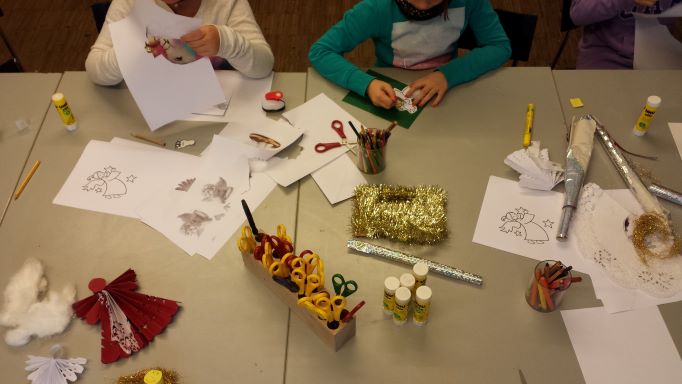 Basteltisch von oben mit Kinderhänden, die an einem Weihnachtsgeschenk arbeiten