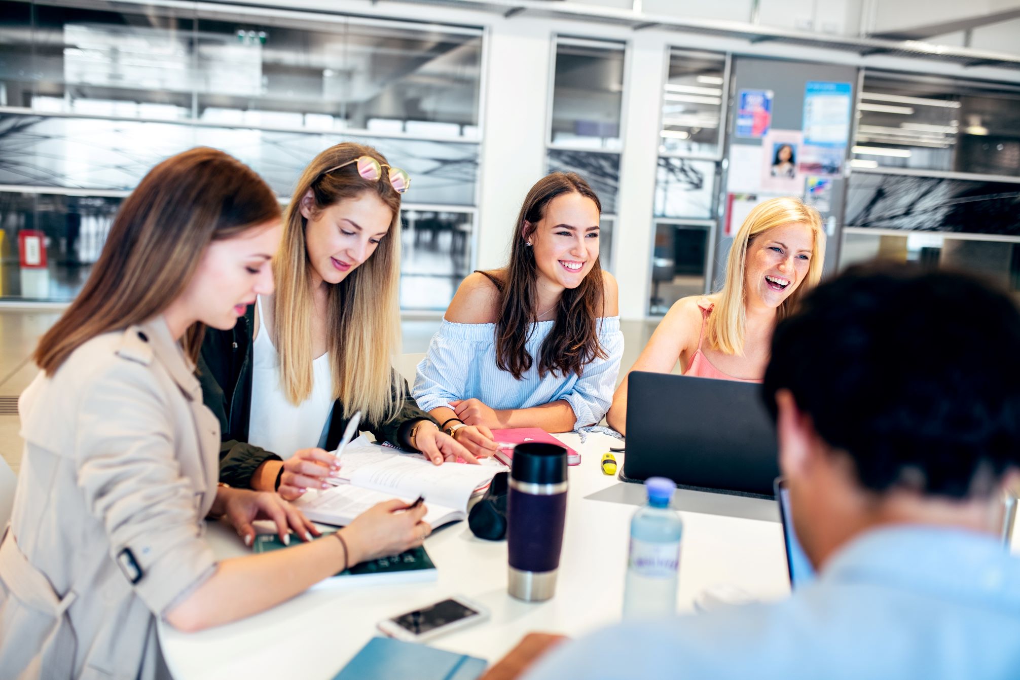 Vier weibliche Studierende an der Uni Klagenfurt, die sich um einen Tisch scharen und austauschen