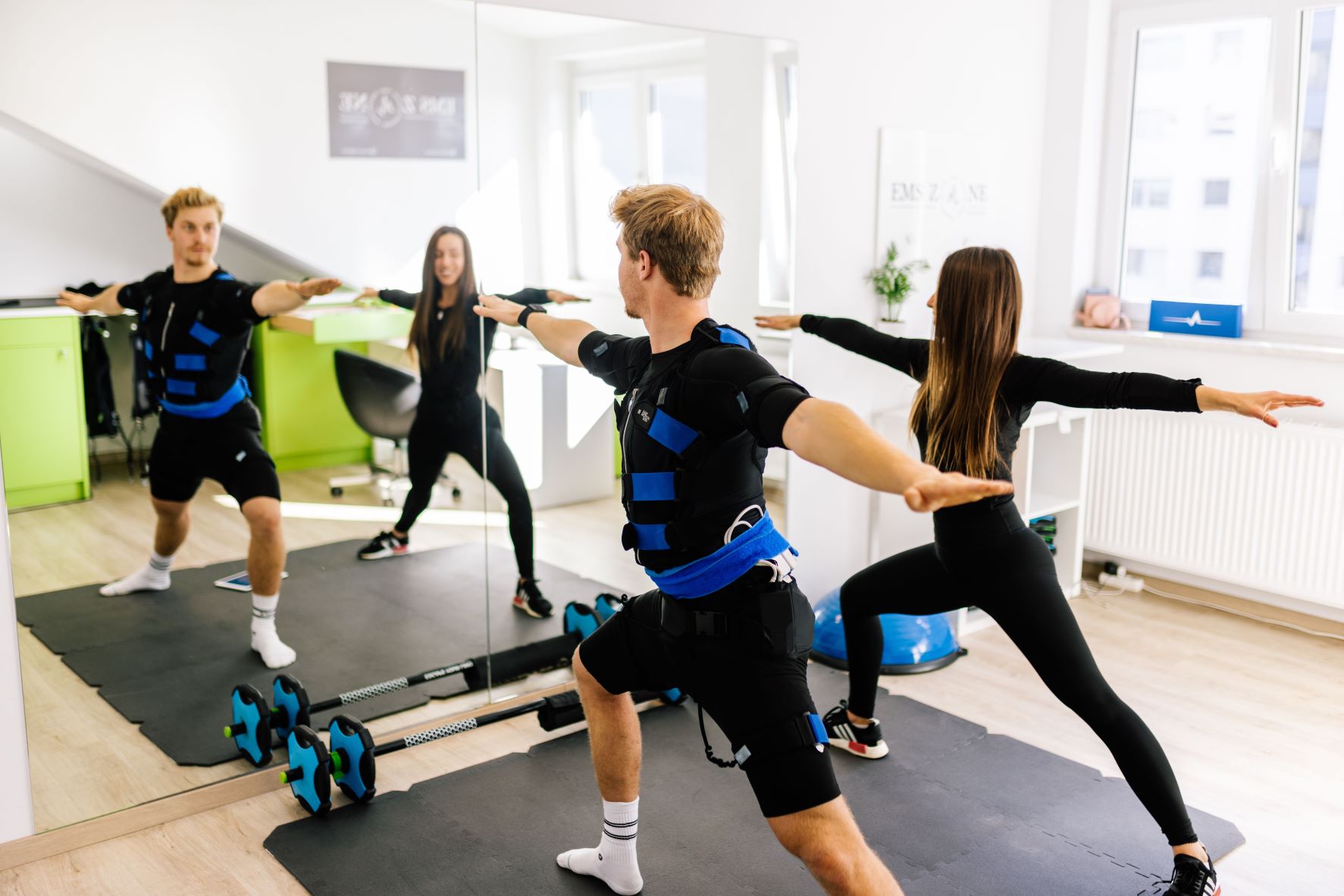 Ein Mann und eine Frau im EMS-Anzug machen Fitnesstraining vor einem Spiegel