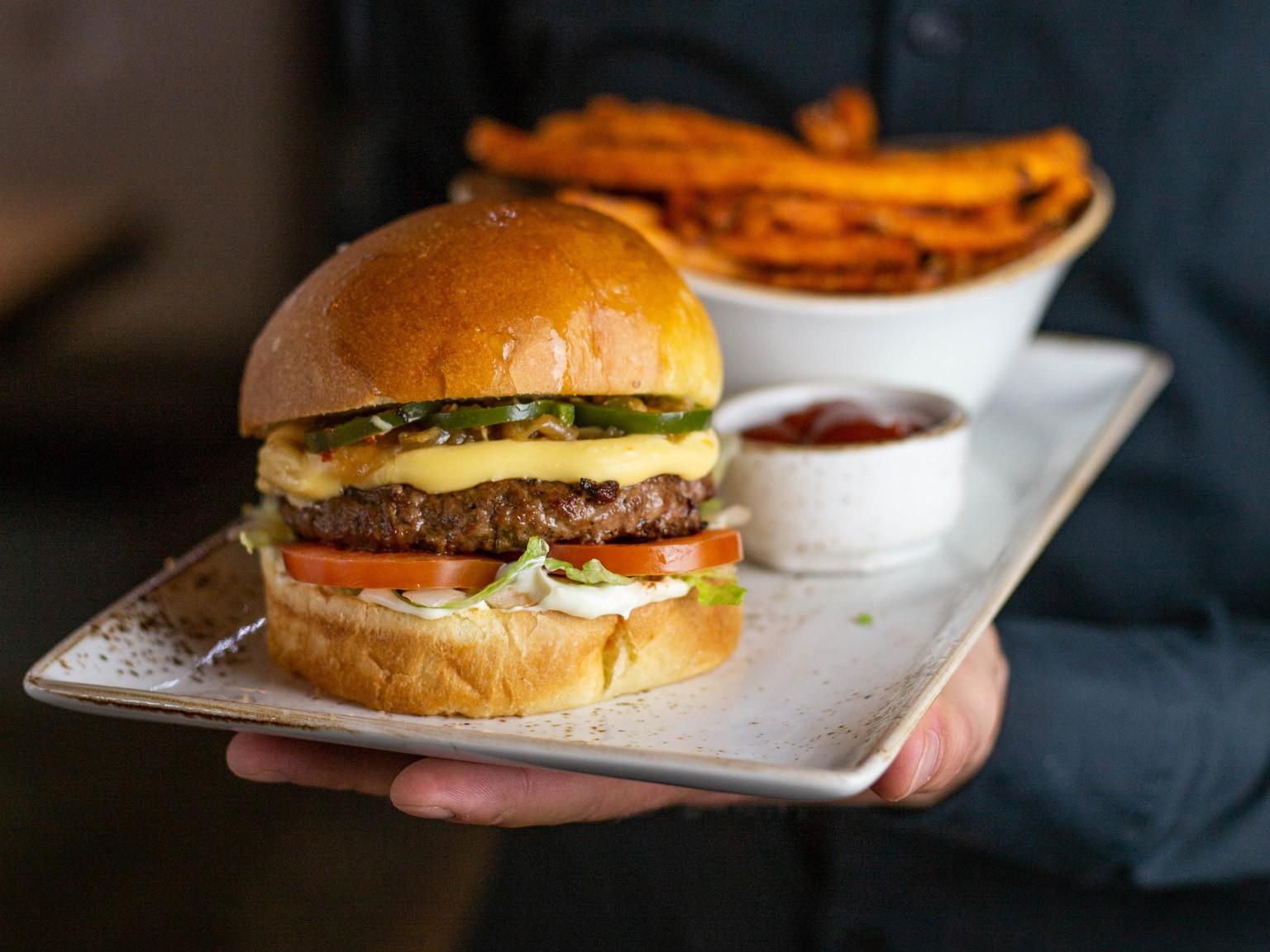 Ein großer Cheeseburger von Freigeist Burger auf einem weißen Teller, daneben Pommes und Ketchup