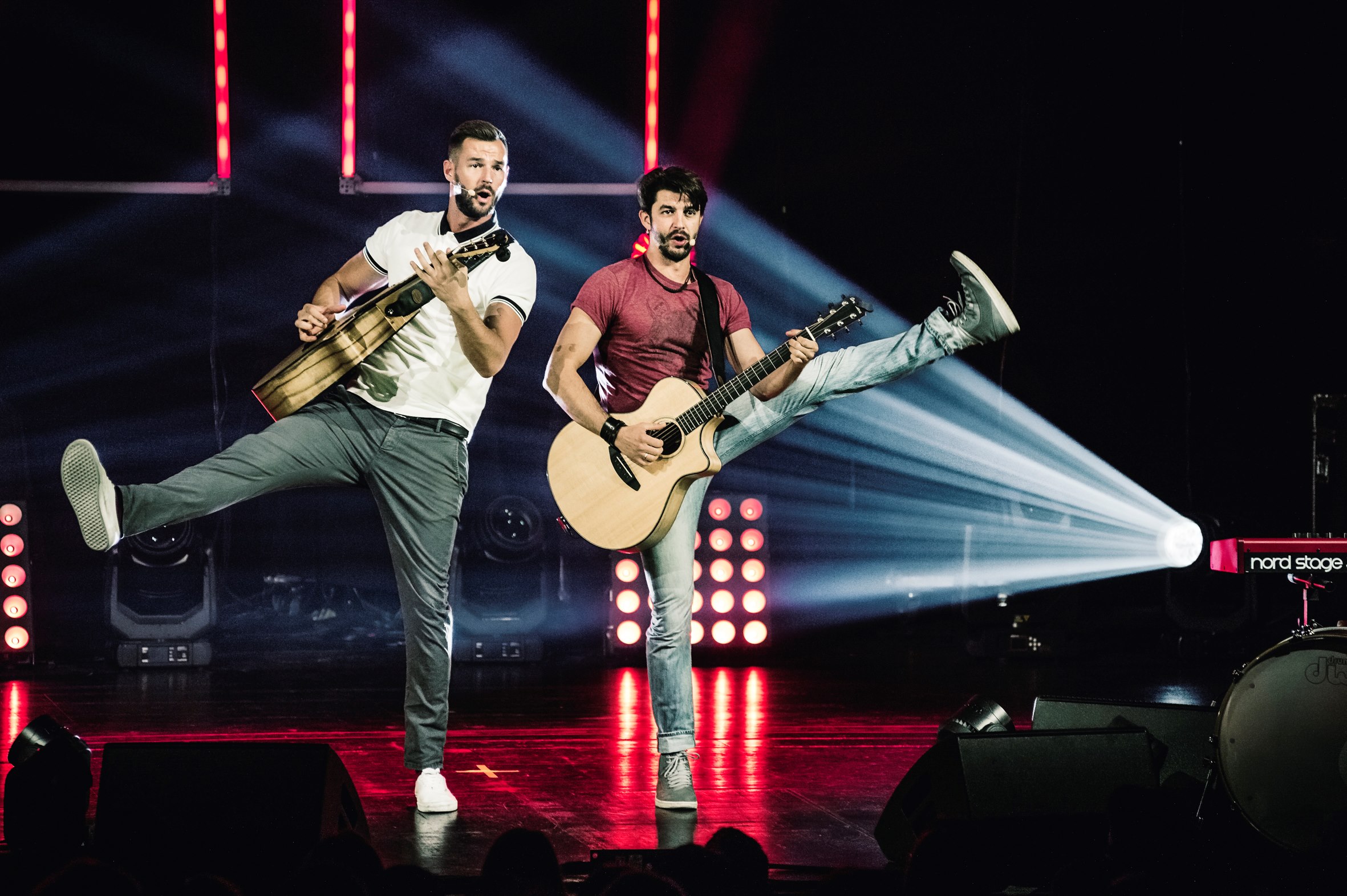 Das PopDuo Pizzera & Jaus mit Gitarren in der Hand und je einem Bein gehoben in Bühnen-Action