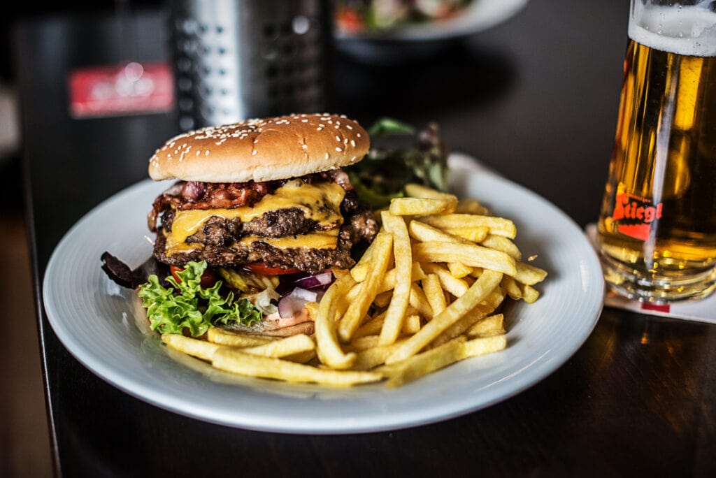 Burger mit Sesambrötchen, Pommes Frites auf einem weißen Teller, wie er im Uni.Wirt in Klagenfurt serviert wird